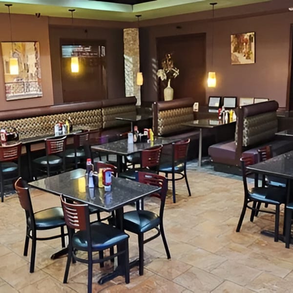Interior of Monroe Grill & Bar with empty tables, chairs, and booths, featuring warm lighting and artwork.