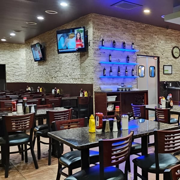 Interior of Monroe Grill & Bar with tables, chairs, TVs, and blue-lit shelves with bottles.