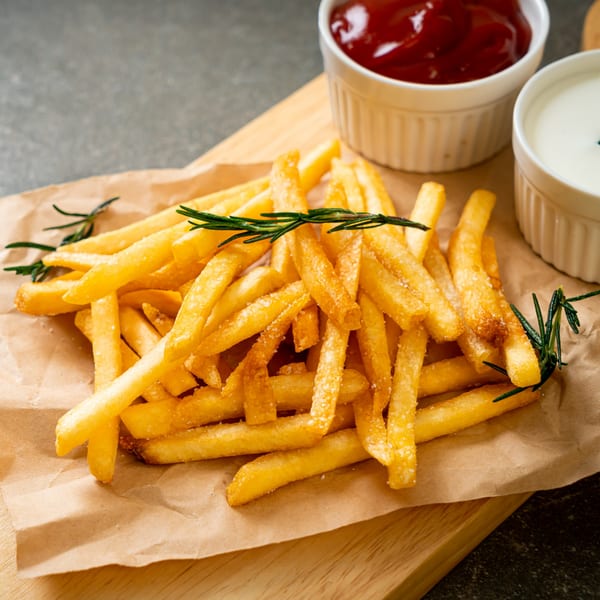 Golden french fries with rosemary sprigs on brown paper, served with ketchup and white sauce.