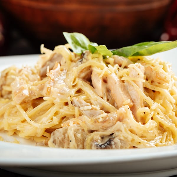 Creamy chicken pasta with grated cheese and a basil leaf on a white plate at Monroe Grill & Bar.